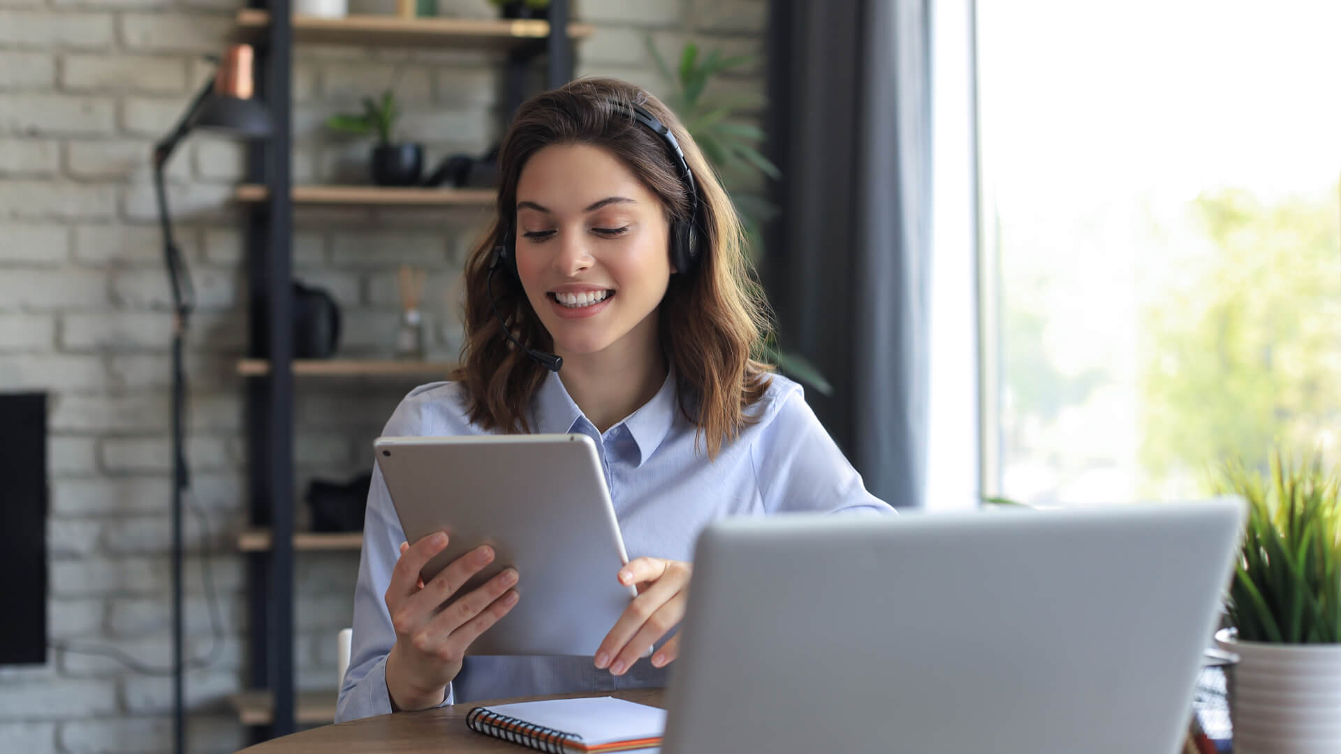 woman at her desk, smiling and looking at a tablet